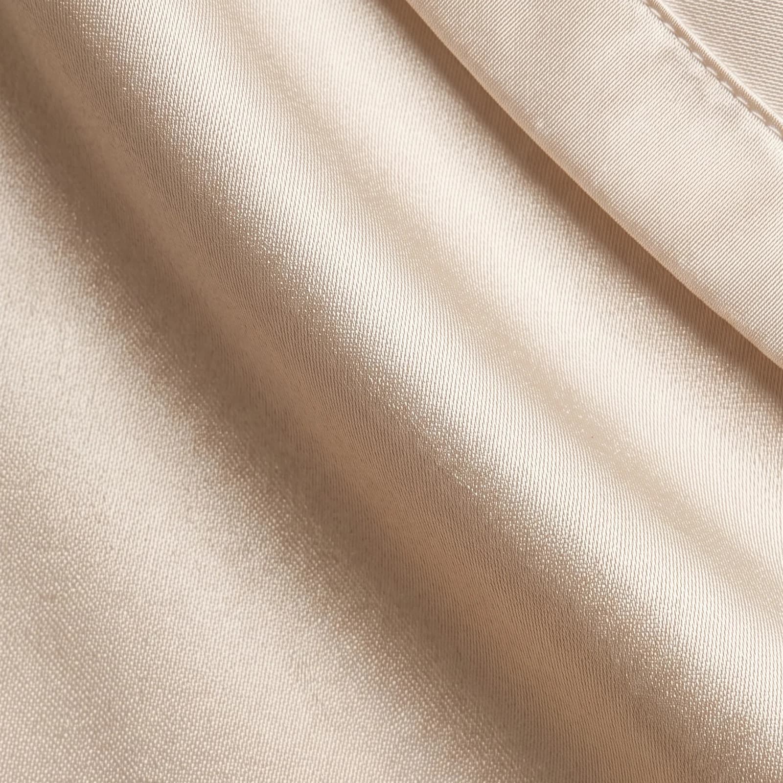 Extreme macro close-up of ivory mulberry silk charmeuse, individual threads visible across a soft fold, with the hemmed envelope-closure edge running through one corner.